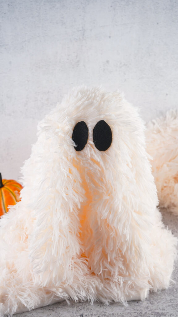 Viral Sherpa Ghost DIY Halloween craft made with fluffy white sherpa fabric, black felt eyes, and a small orange pumpkin.
