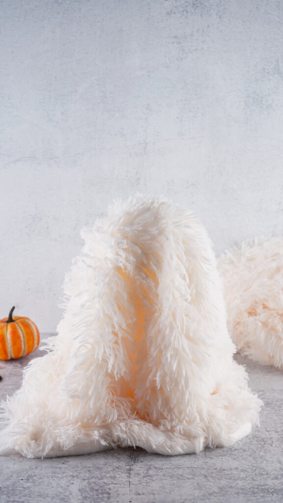 Viral Sherpa Ghost DIY Halloween craft made with fluffy white sherpa fabric, black felt eyes, and a small orange pumpkin.