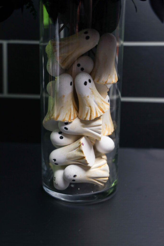 Close-up of small white ghosts with black eyes and metallic gold accents stacked inside a clear glass Halloween vase.