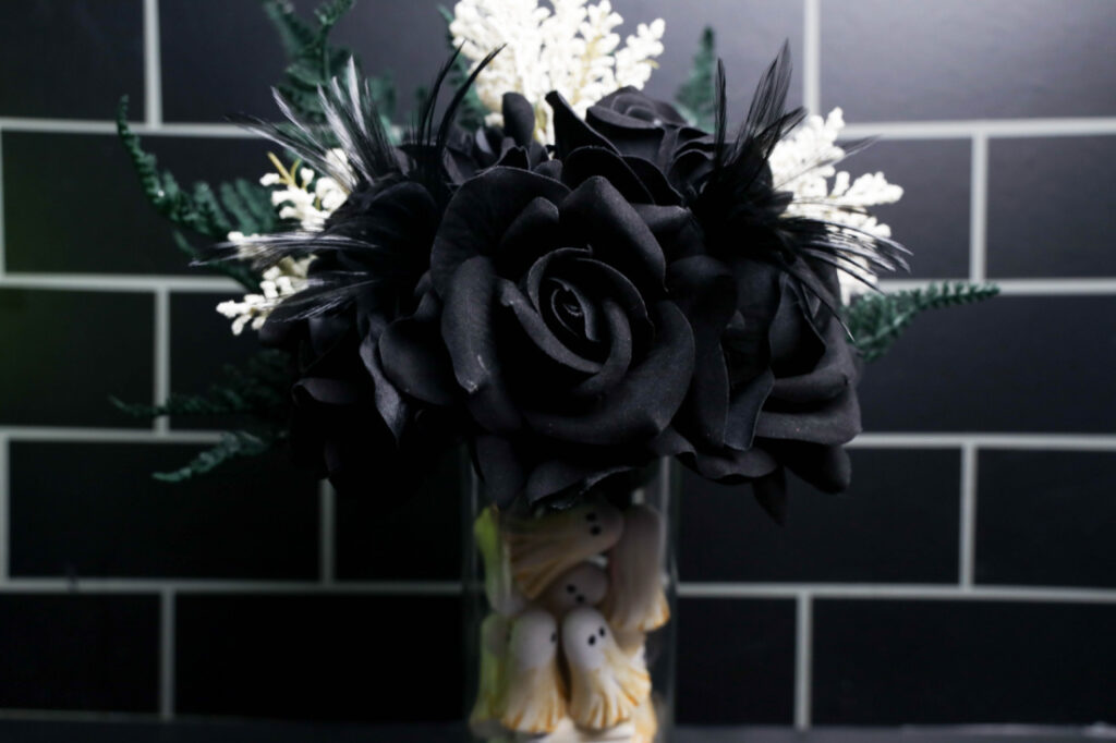 Close-up of small white ghosts with black eyes and metallic gold accents stacked inside a clear glass Halloween vase.