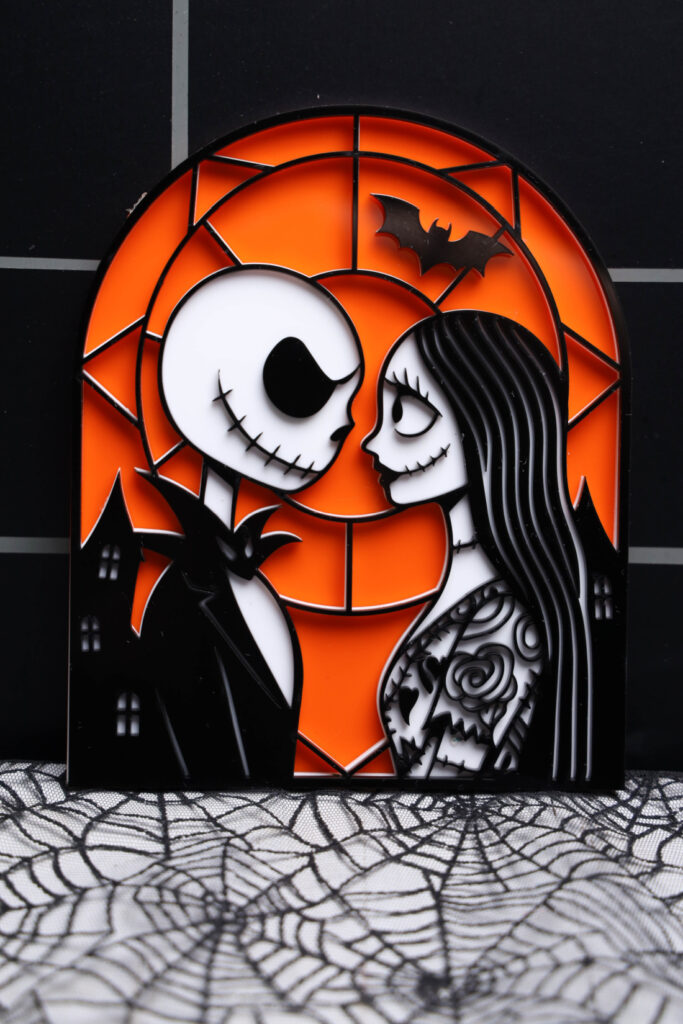layered Jack and Sally acrylic decoration with an orange background and black outlines, resting on spiderweb fabric.