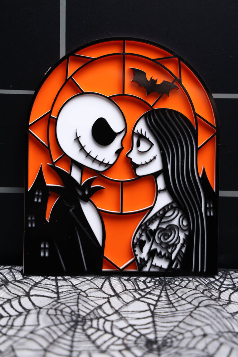 layered Jack and Sally acrylic decoration with an orange background and black outlines, resting on spiderweb fabric.
