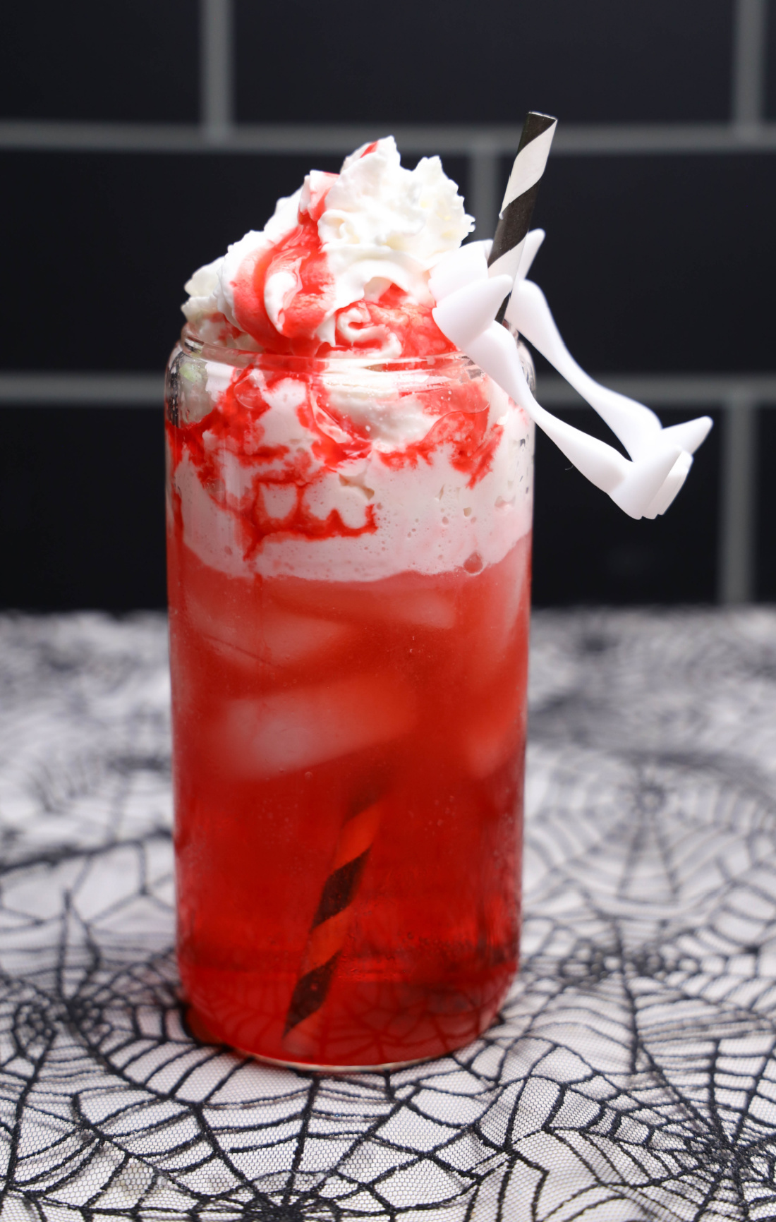Red Vampire Dirty Soda over ice with whipped topping, strawberry syrup, a striped straw, and white plastic fangs.